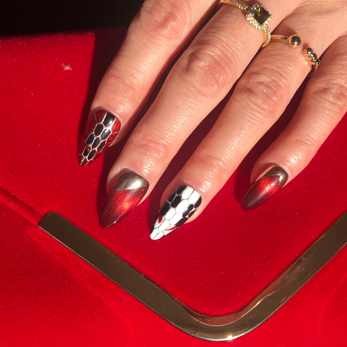 Close up of a hand wearing press-on nails featuring snakeskin design in red, gold, black and white. 