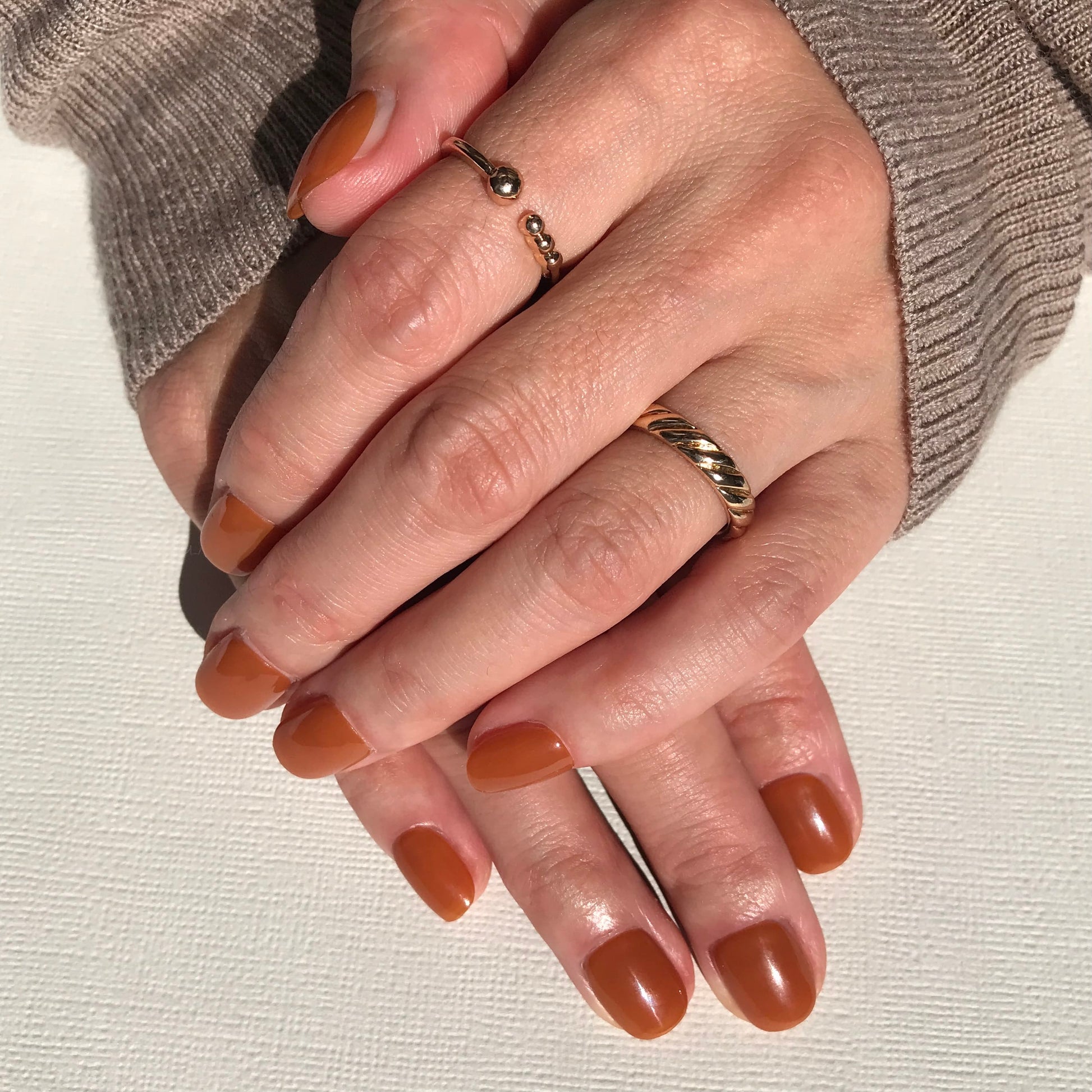 Hands modelling salon quality press-on nails in high gloss rich caramel.