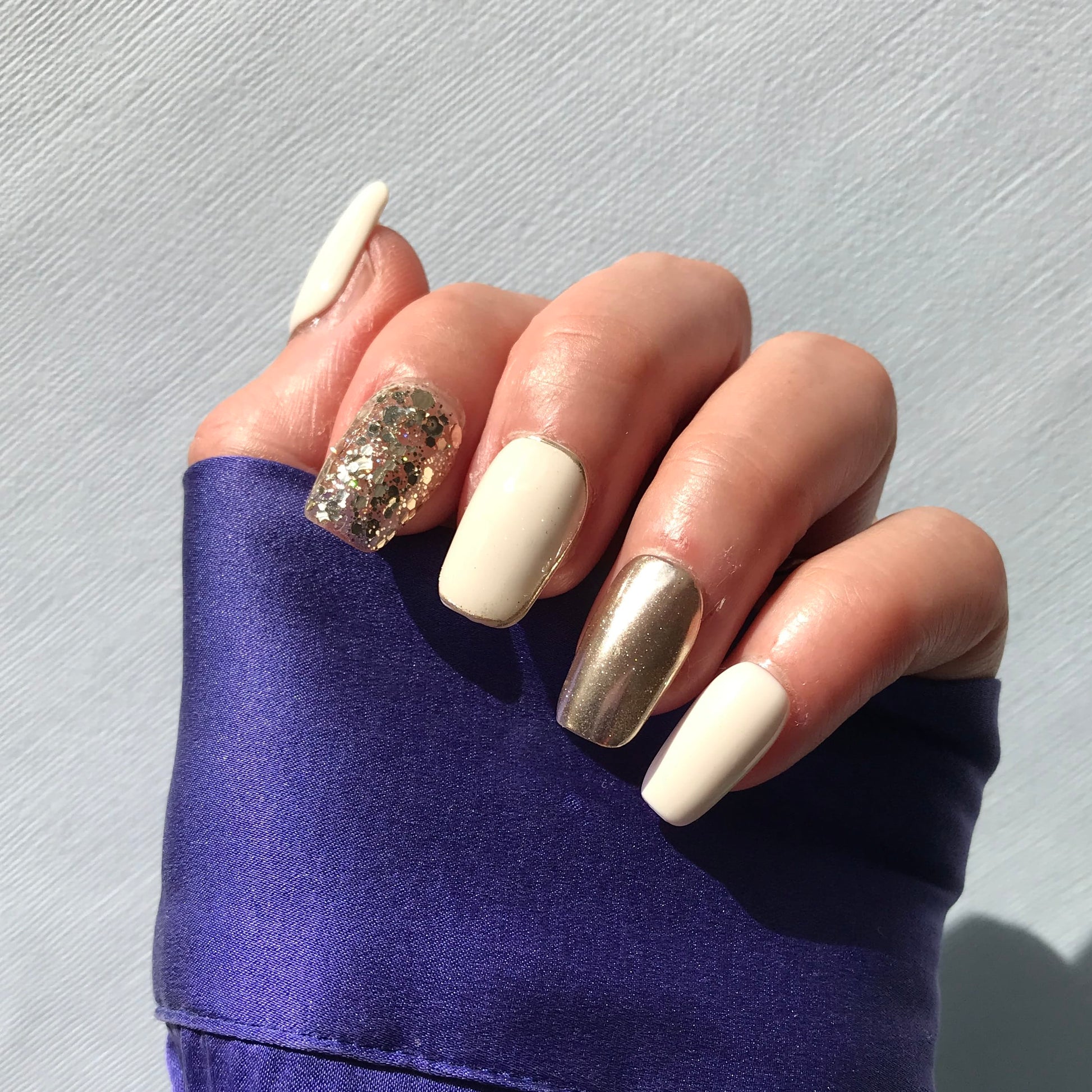 Hand with premium handmade press-on nails in white, gold with gold glitter detail.