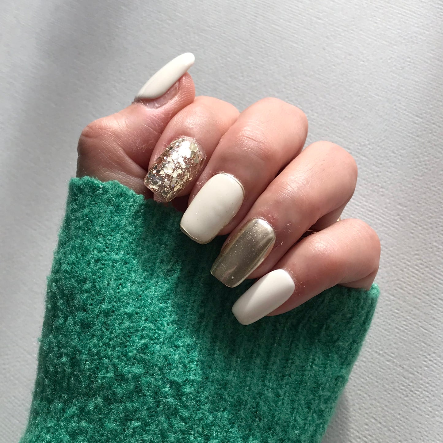 Close-up of a hand with white and gold press-on nails. 